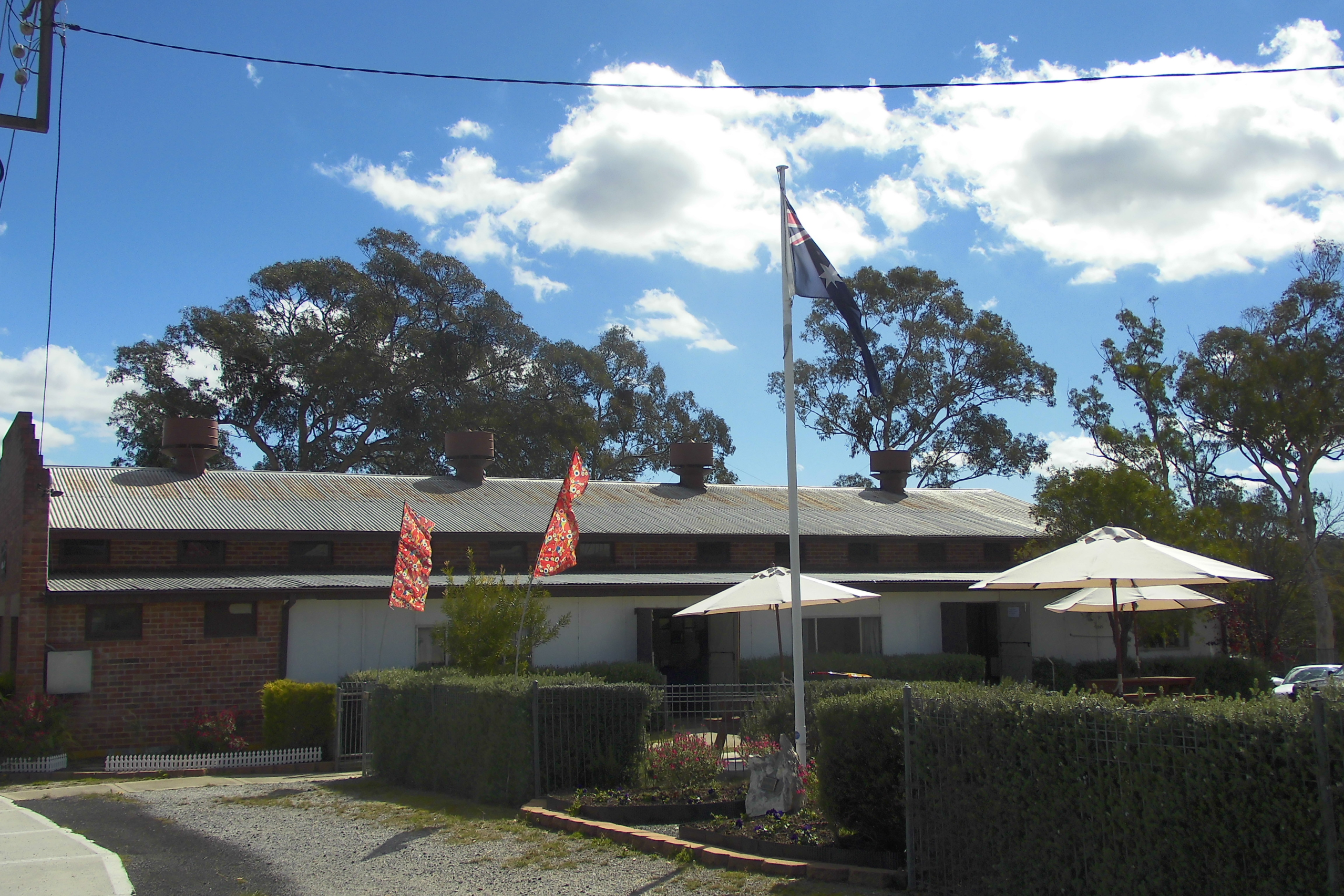 Picture of Capertee Hall from eastern side with Australian flag on a flagpole and some market flags also flying and 2 shade umbrellas in the foreground.