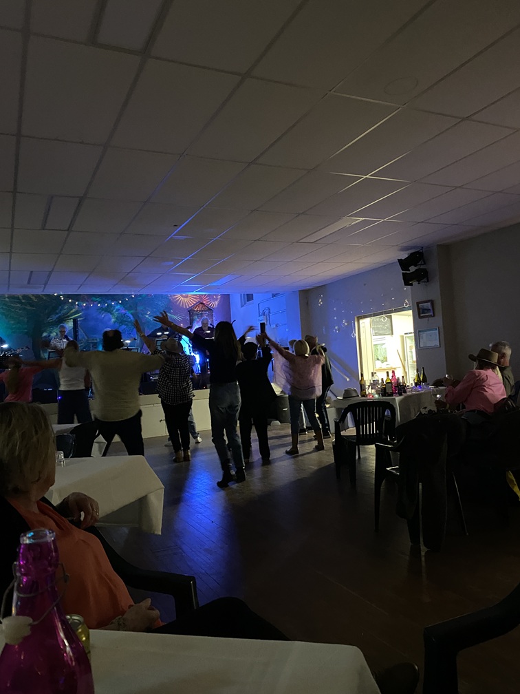 Capertee Progress October 2025 Dance night with Bushrock at Capertee Memorial Hall. Bushrock is on stage with coloured party lighting, there is a people dancing in the middle and people seated at tables in at the foreground.